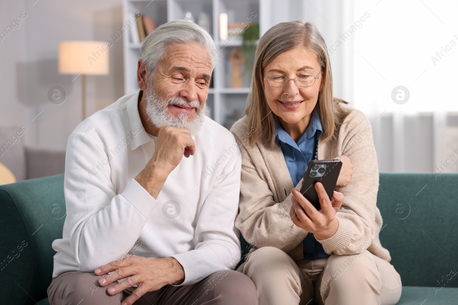 Photo of Happy elderly couple with smartphone on sofa at home