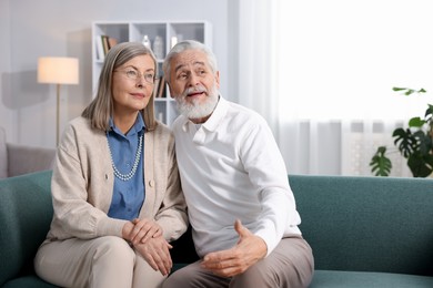 Photo of Cute elderly couple on sofa at home. Space for text