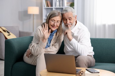 Photo of Happy elderly couple having video call by laptop on sofa at home