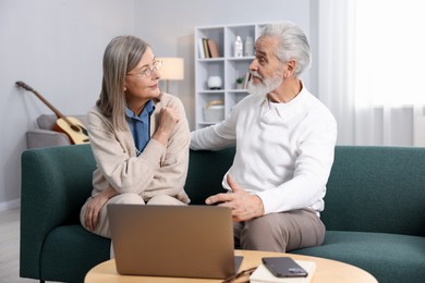 Cute elderly couple looking at each other on sofa at home