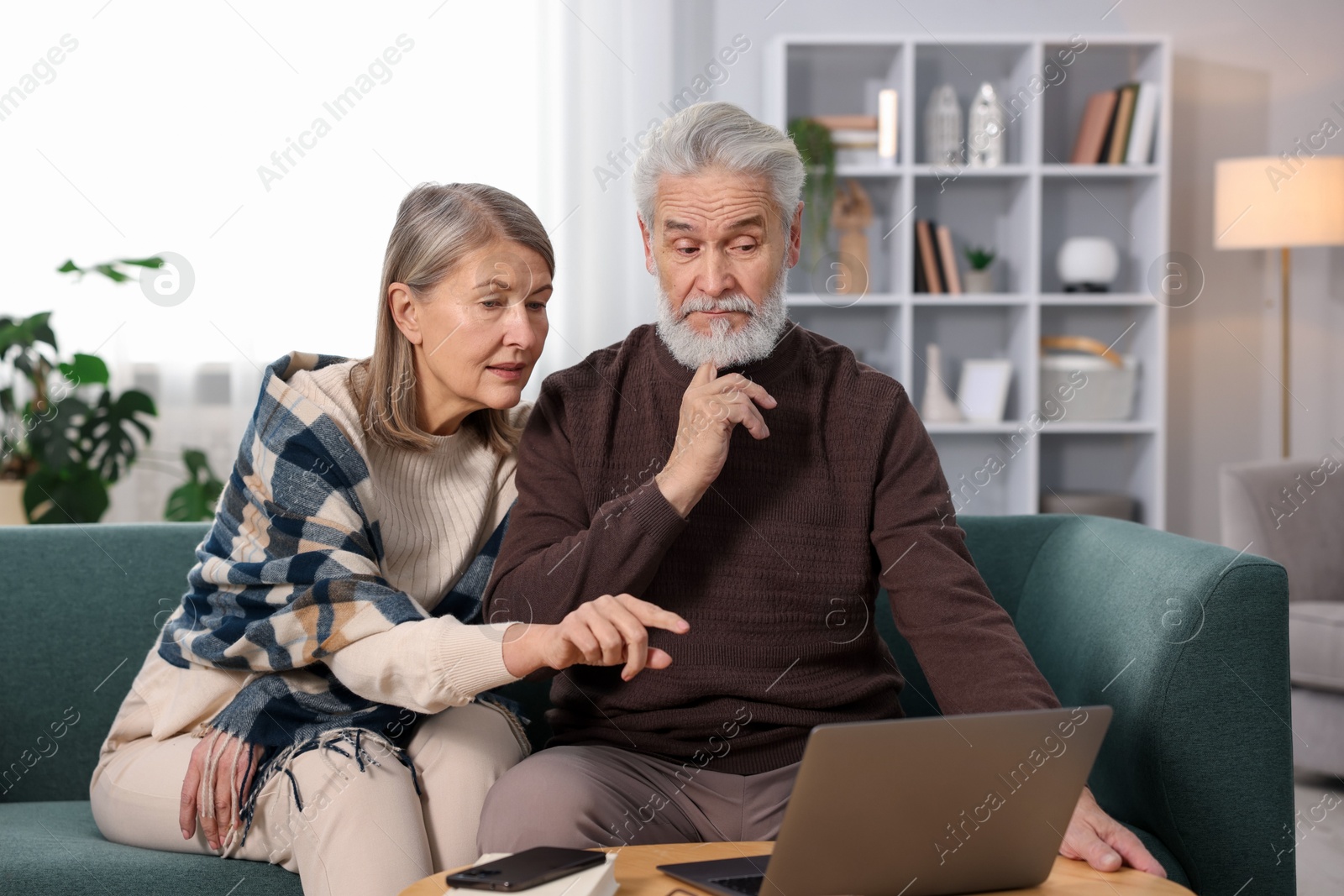 Photo of Cute elderly couple looking at laptop on sofa at home