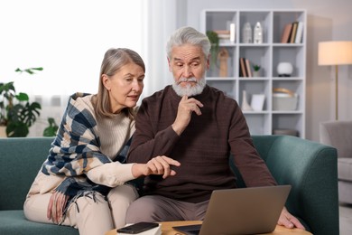 Cute elderly couple looking at laptop on sofa at home