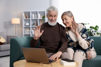 Photo of Happy elderly couple having video call by laptop on sofa at home