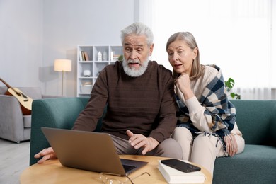 Surprised elderly couple looking at laptop on sofa at home