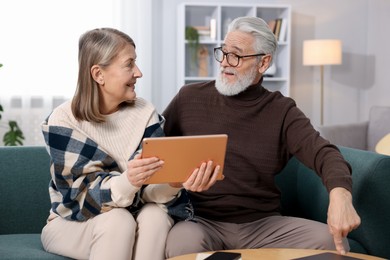 Cute elderly couple looking at tablet on sofa at home