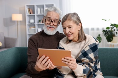 Happy elderly couple looking at tablet on sofa at home