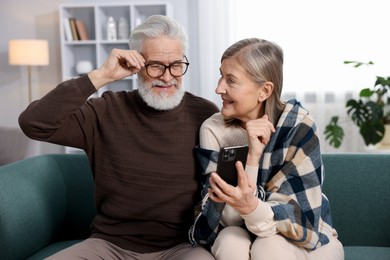 Photo of Happy elderly couple looking at smartphone on sofa at home