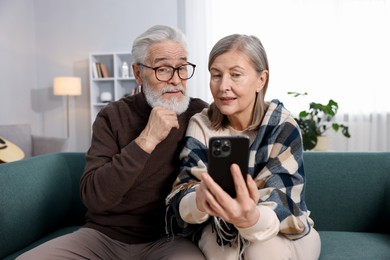 Photo of Happy elderly couple looking at smartphone on sofa at home