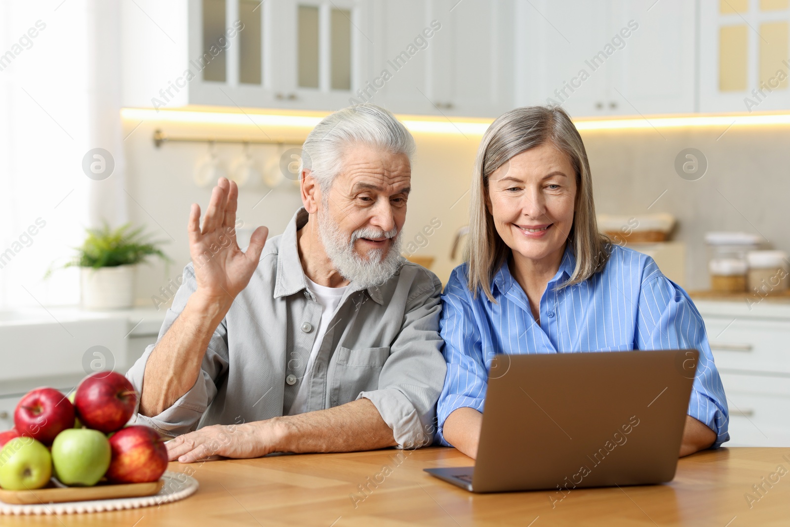 Photo of Happy elderly couple having video call by laptop at table in kitchen