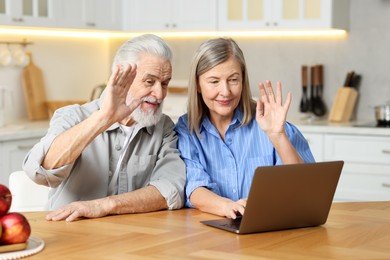 Photo of Cute elderly couple having video call by laptop at table in kitchen