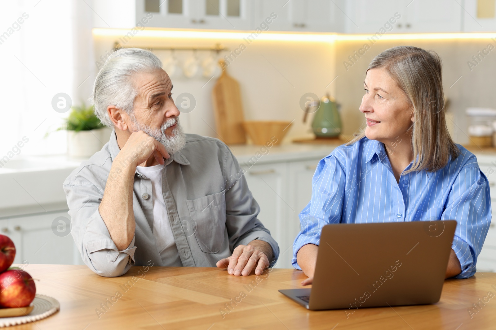 Photo of Cute elderly couple looking at each other at table in kitchen