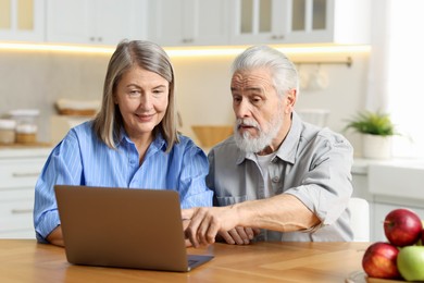 Photo of Cute elderly couple with laptop at table in kitchen