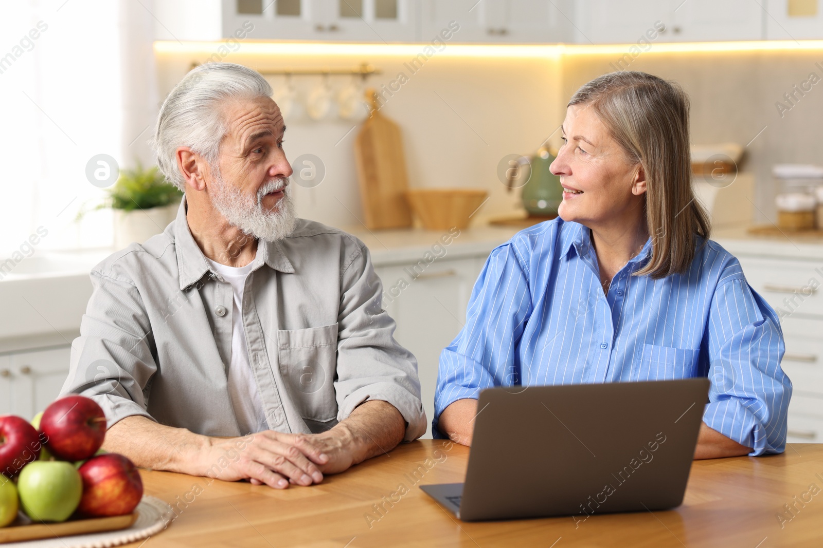 Photo of Cute elderly couple looking at each other at table in kitchen