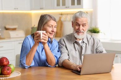 Cute elderly couple with laptop at table in kitchen