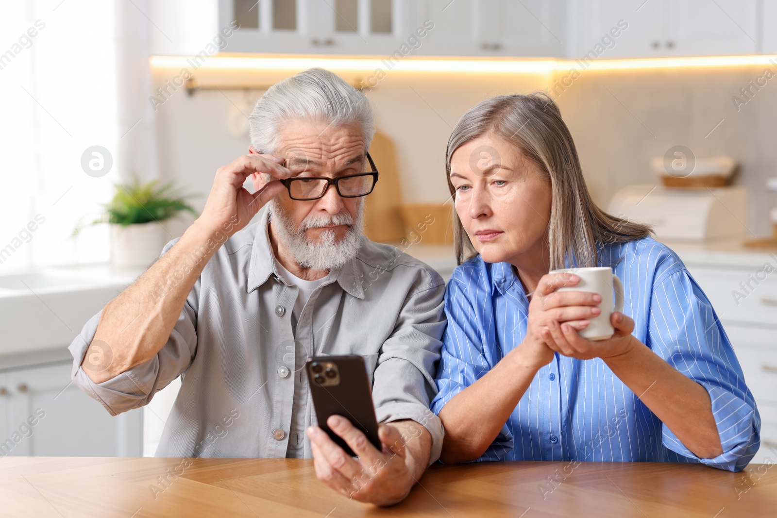 Photo of Cute elderly couple with smartphone at table in kitchen