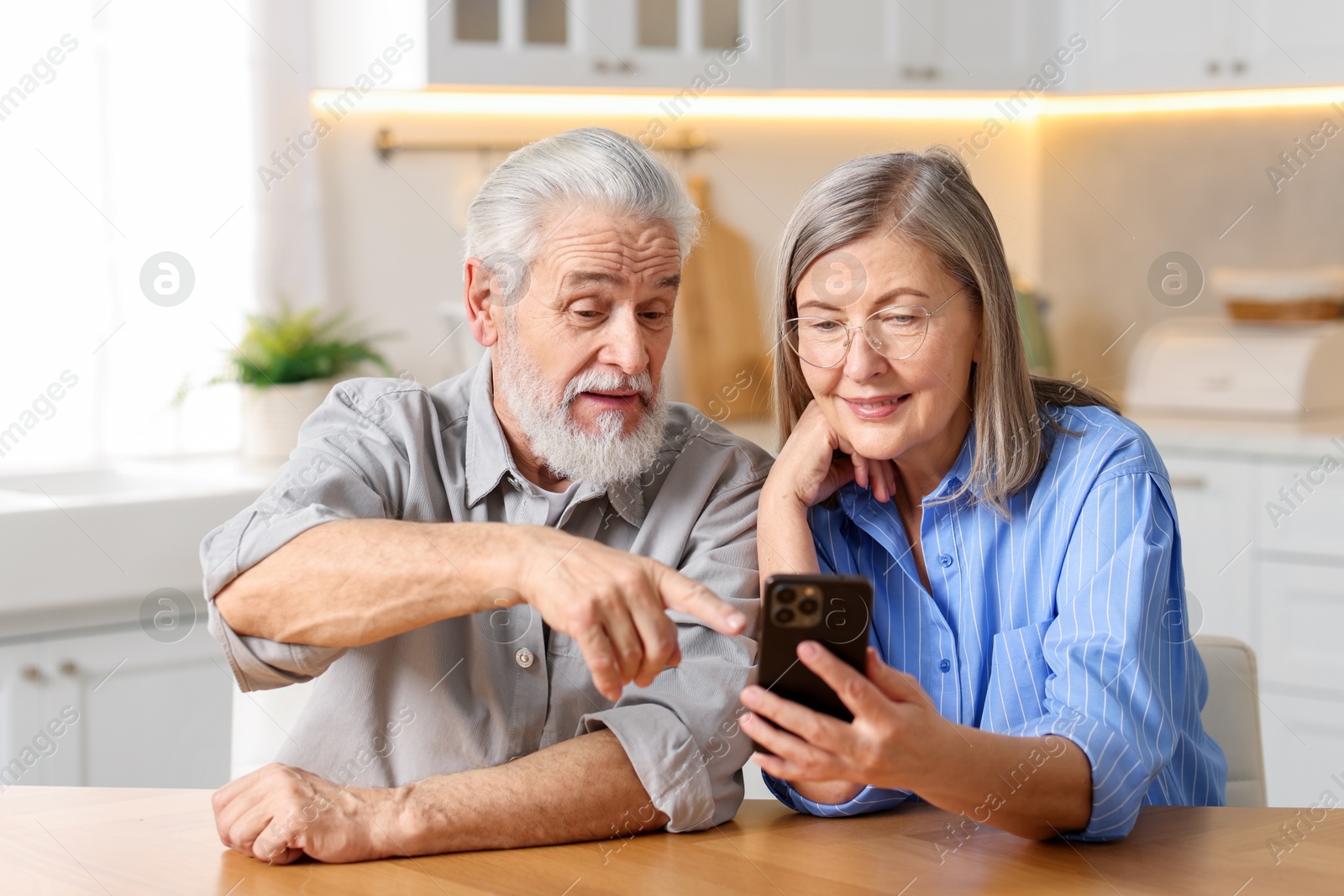 Photo of Cute elderly couple with smartphone at table in kitchen