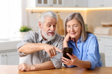 Photo of Cute elderly couple with smartphone at table in kitchen