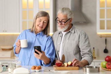 Photo of Cute elderly couple with smartphone at table in kitchen