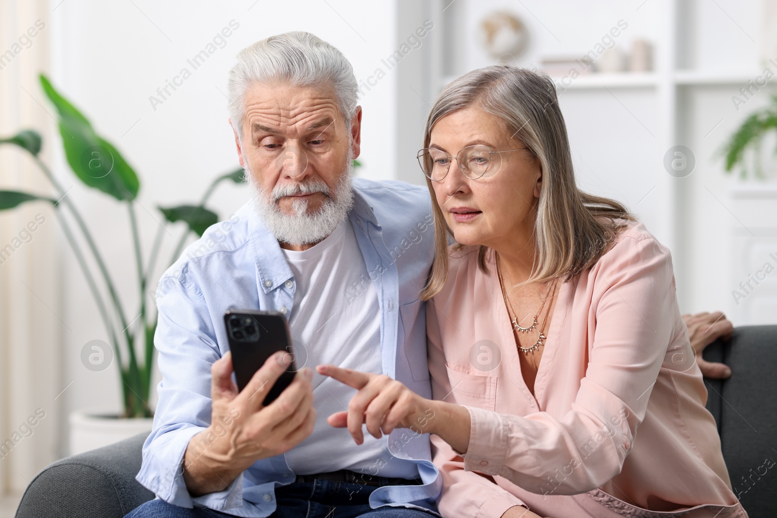 Photo of Cute elderly couple looking at smartphone on sofa at home