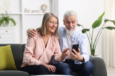 Happy elderly couple looking at smartphone on sofa at home