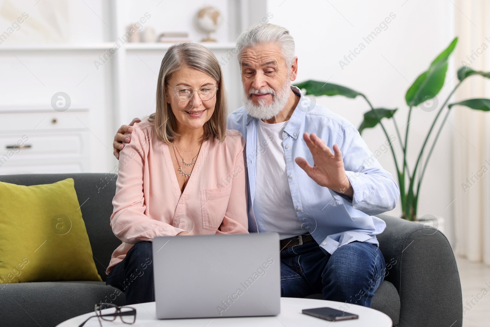 Photo of Happy elderly couple having video call by laptop on sofa at home