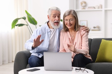 Photo of Happy elderly couple having video call by laptop on sofa at home