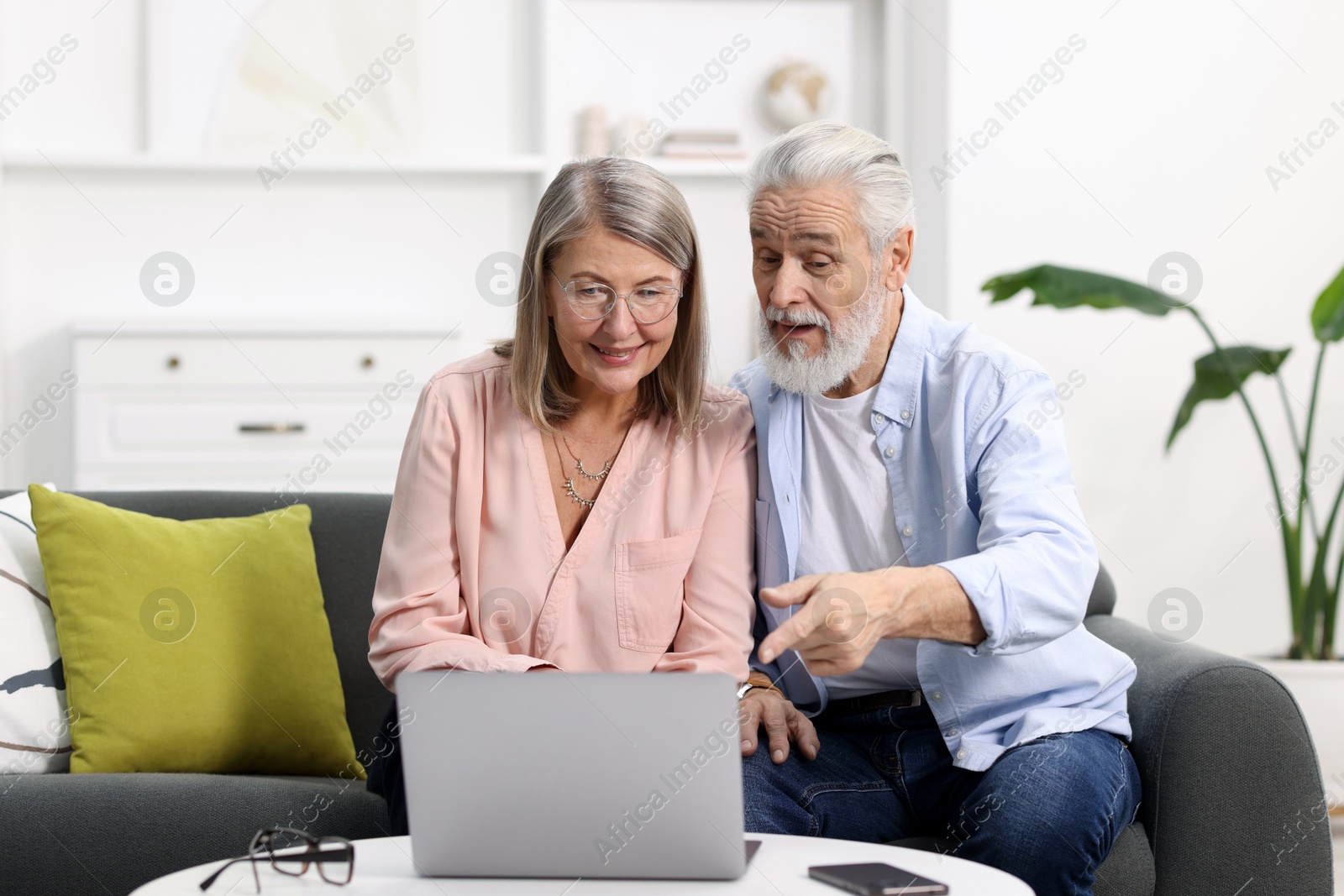 Photo of Happy elderly couple looking at laptop on sofa at home