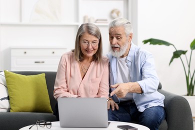 Happy elderly couple looking at laptop on sofa at home