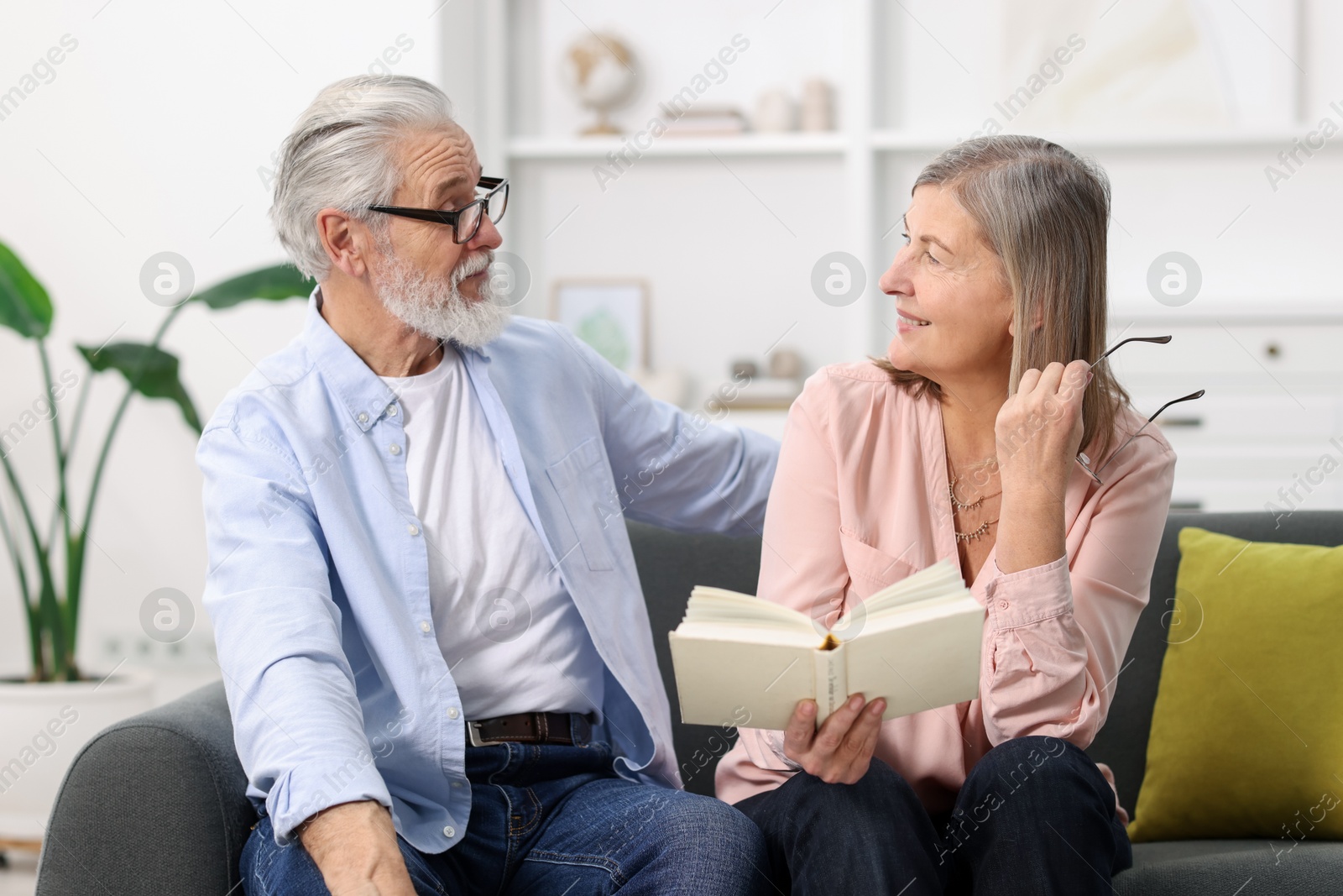 Photo of Cute elderly couple reading book together on sofa at home