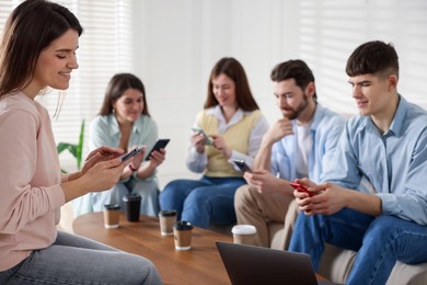 Photo of Internet addiction. Group of friends with gadgets and coffee at table indoors