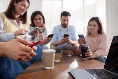 Photo of Internet addiction. Group of friends with gadgets and coffee at table indoors