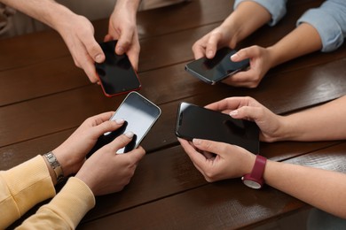 Photo of Internet addiction. People with smartphones at wooden table, closeup