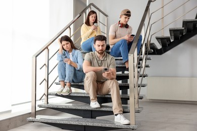 Internet addiction. Group of people with smartphones on stairs indoors