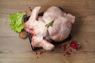 Photo of Whole raw turkey, marinade, cranberries and lettuce on wooden table, flat lay