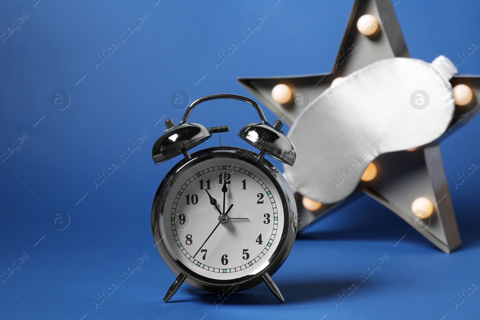 Photo of Alarm clock, sleep mask and star shaped night lamp on blue background. Time for sleeping