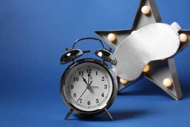 Photo of Alarm clock, sleep mask and star shaped night lamp on blue background. Time for sleeping