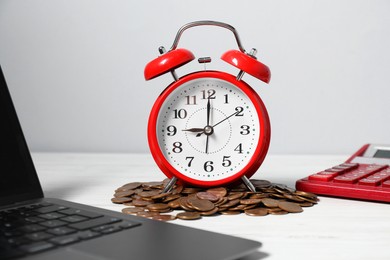 Photo of Alarm clock, coins, laptop and calculator on white wooden table. Tax time