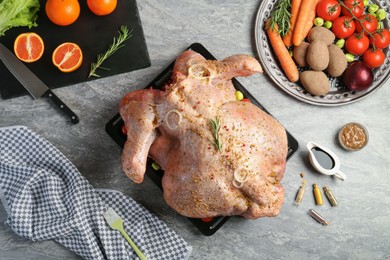 Whole raw turkey with ingredients for marinade and other products on grey table, flat lay