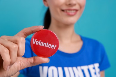 Photo of Woman showing red button badge with word Volunteer on light blue background, closeup