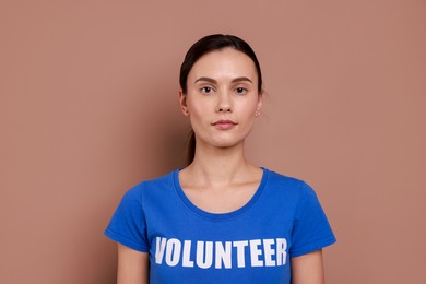 Young beautiful woman wearing t-shirt with printed word Volunteer on light brown background