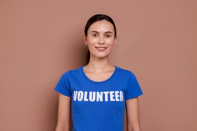 Photo of Young beautiful woman wearing t-shirt with printed word Volunteer on light brown background