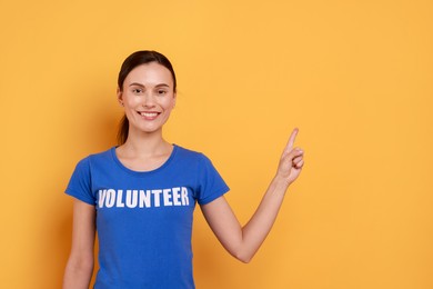 Photo of Young beautiful volunteer in t-shirt with printed word pointing at something on orange background