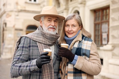 Family portrait of happy elderly couple with paper cups on city street