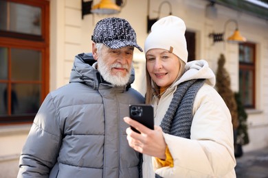 Happy elderly couple with smartphone on city street