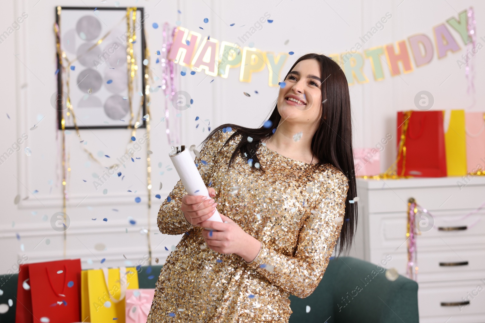 Photo of Happy woman blowing up confetti popper in room decorated for party