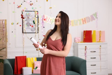 Photo of Happy woman blowing up confetti popper in room decorated for party