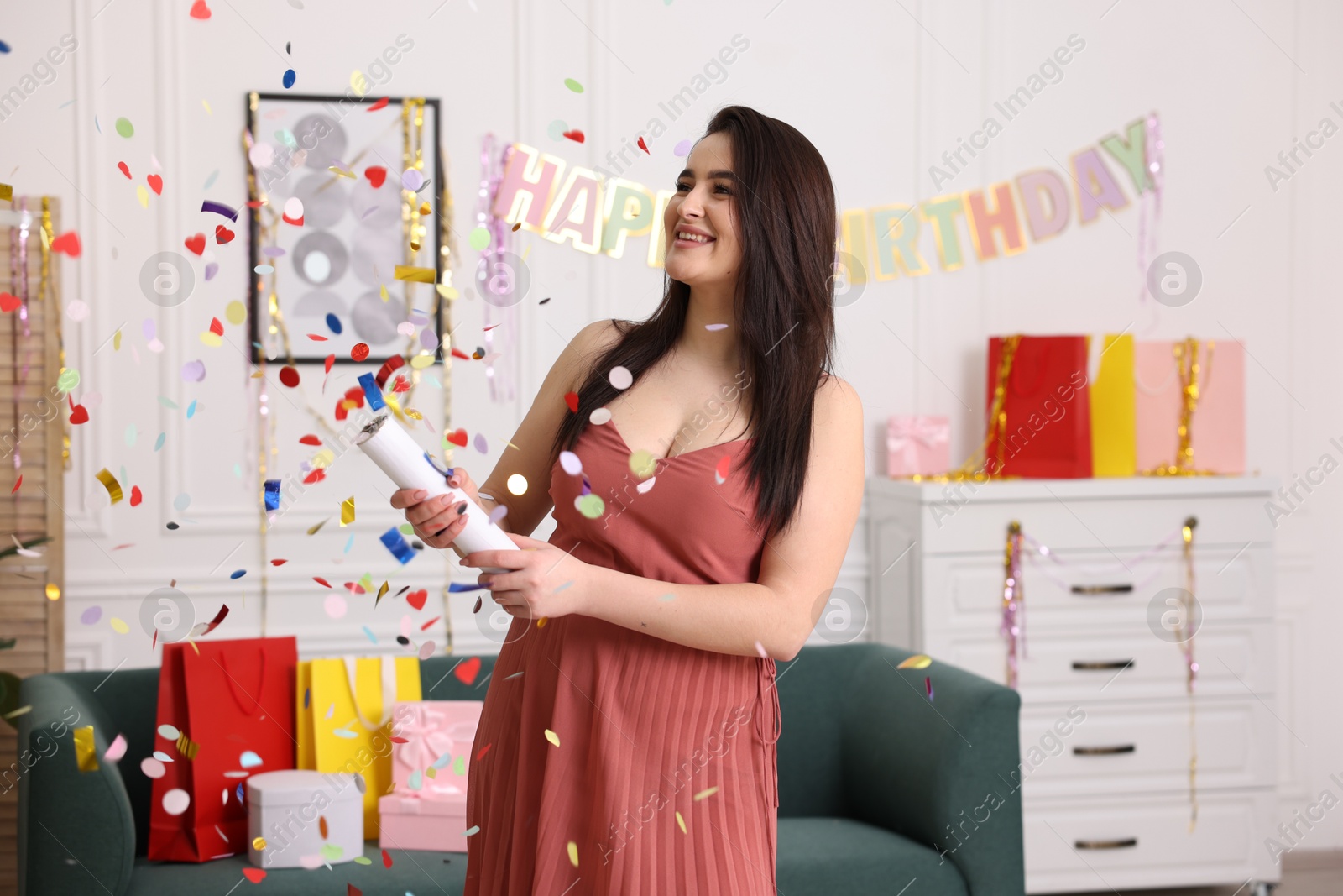 Photo of Happy woman blowing up confetti popper in room decorated for party