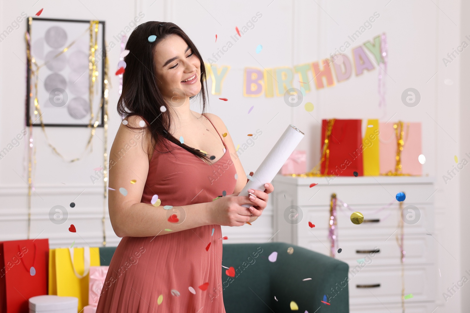 Photo of Happy woman blowing up confetti popper in room decorated for party