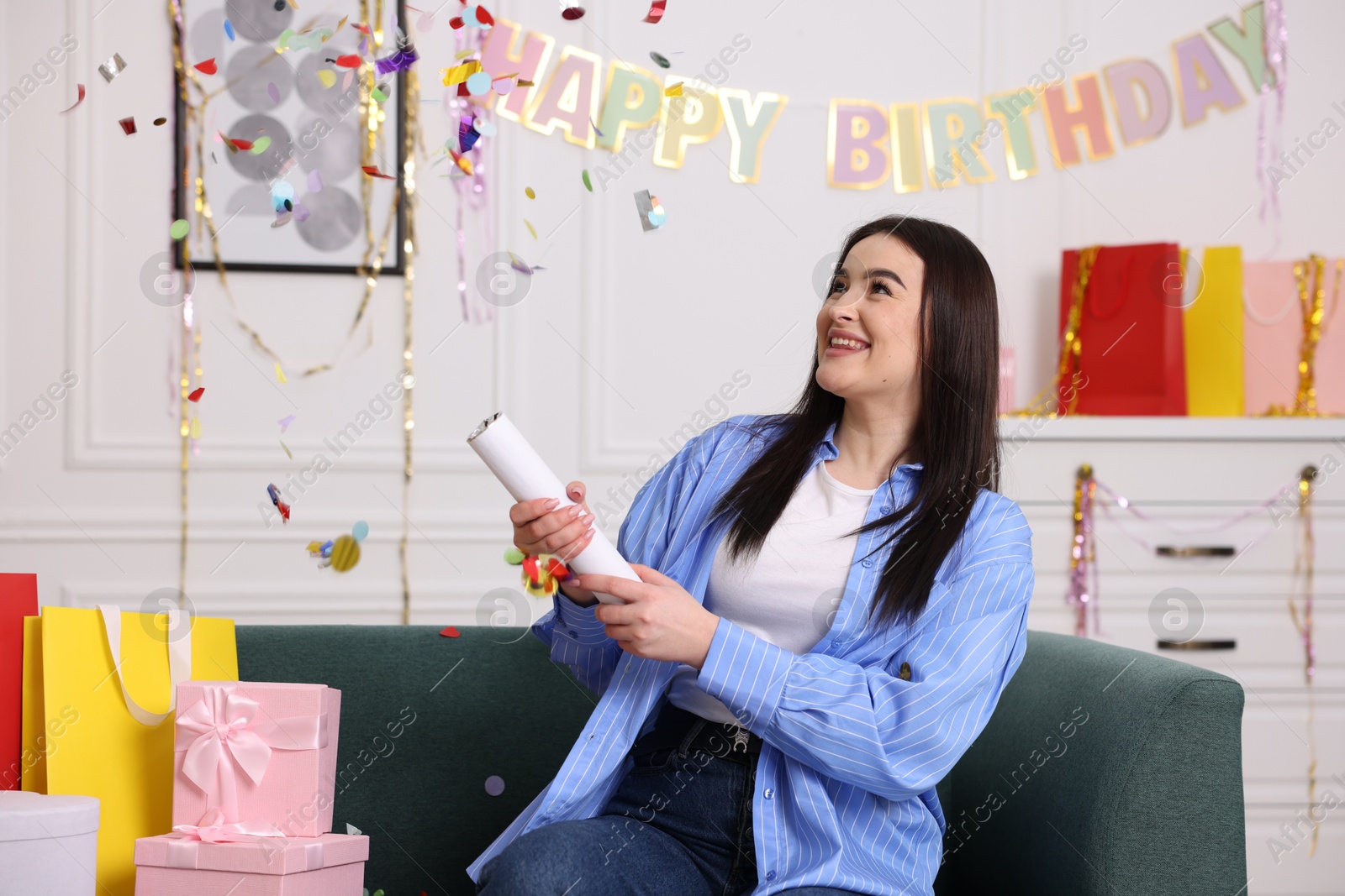 Photo of Happy woman blowing up confetti popper on sofa at home