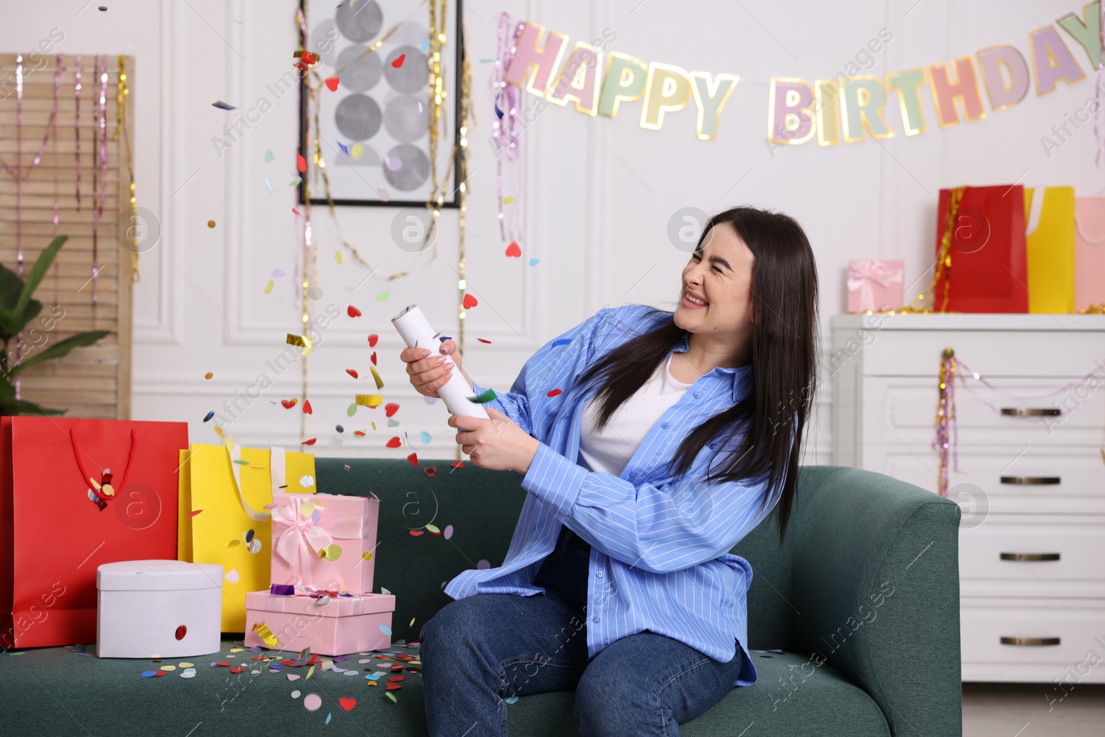 Photo of Happy woman blowing up confetti popper on sofa at home